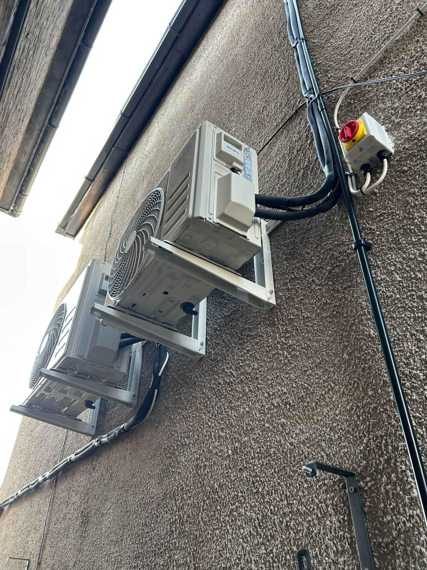 Two outdoor air conditioning units on wall brackets viewed from below